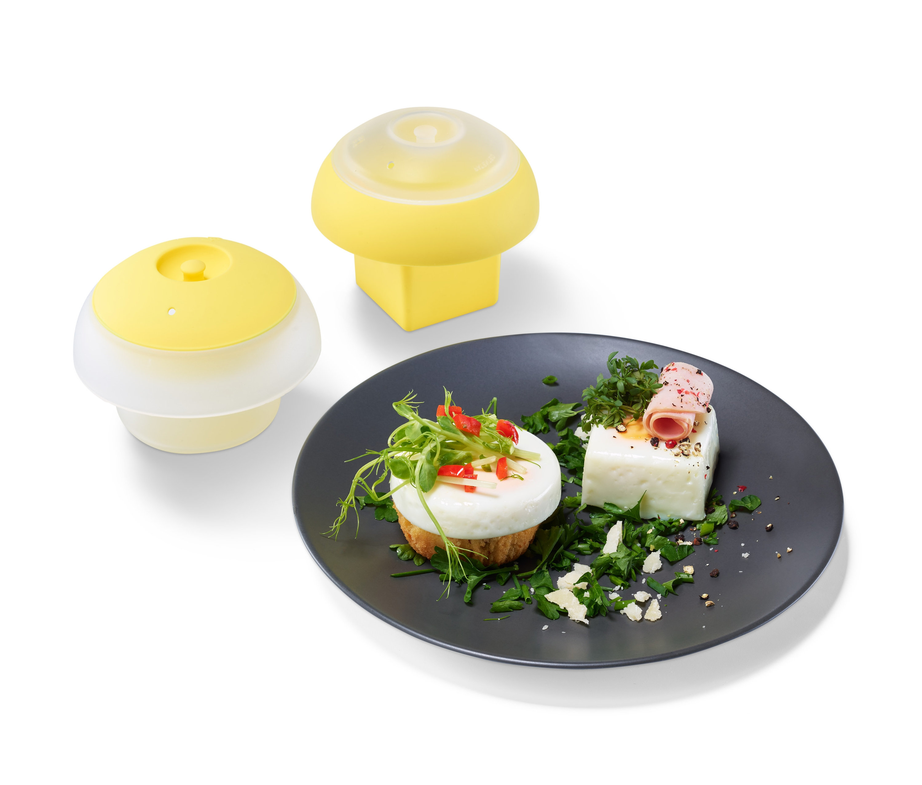 Dwa żółte zestawy foremek do jajek i talerz z jajkami ozdobionymi zielenią.