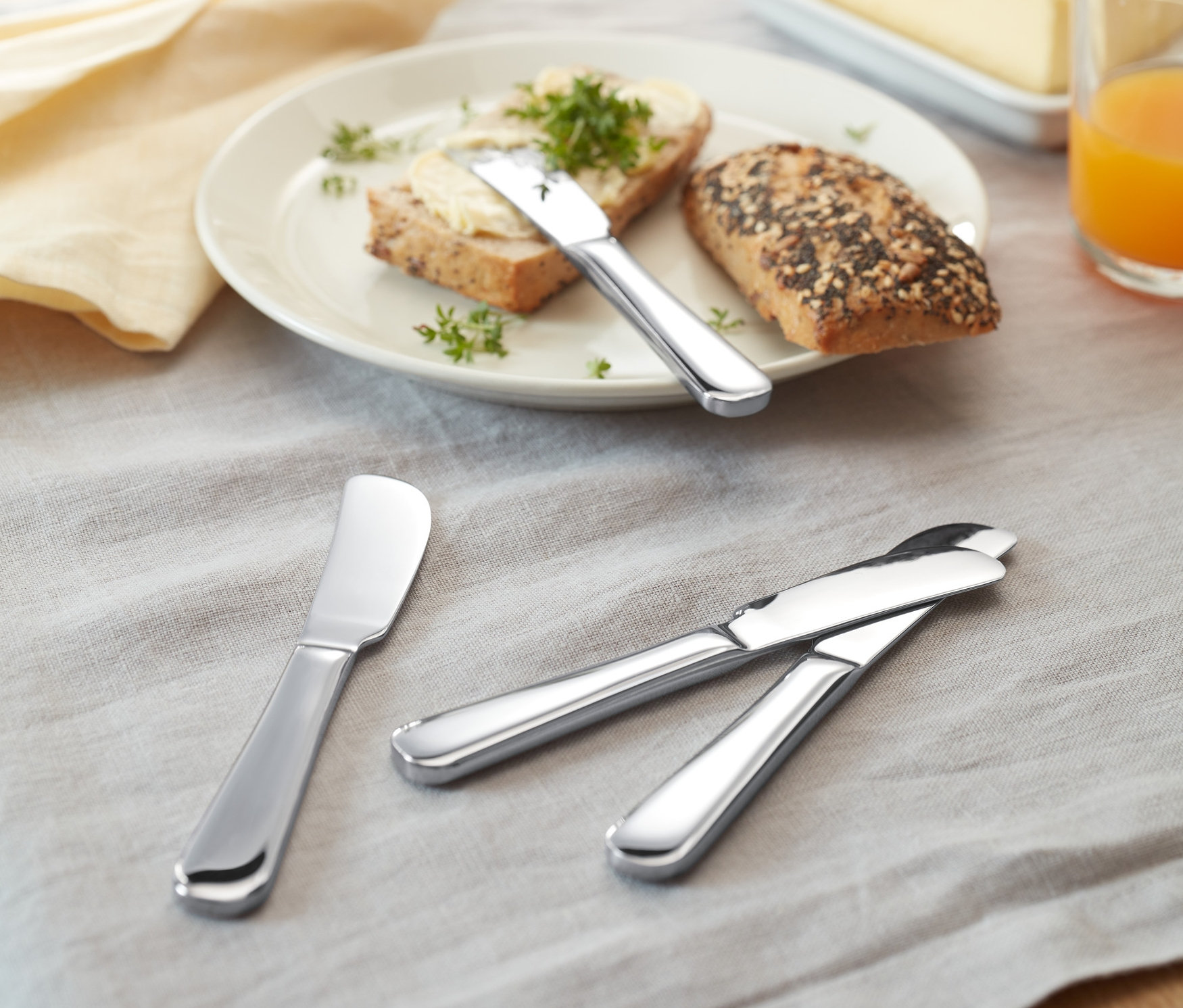 Na stole leżą chleby z masłem i 4 noże do masła.