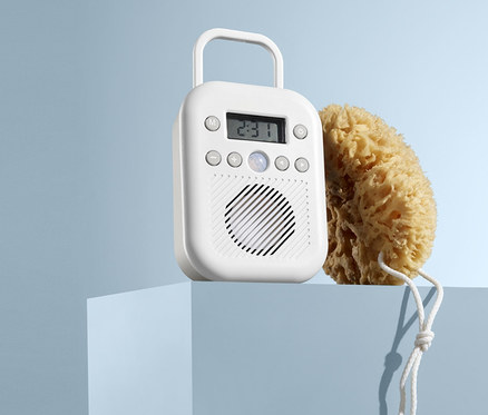 Na niebieskim postumencie stoi białe radio łazienkowe i naturalna gąbka do mycia.