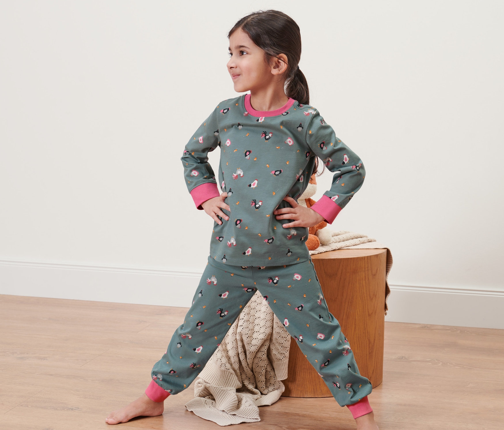 Dziewczynka stoi z rękami na biodrach w piżamie dziecięcej, błękitno-szarej.