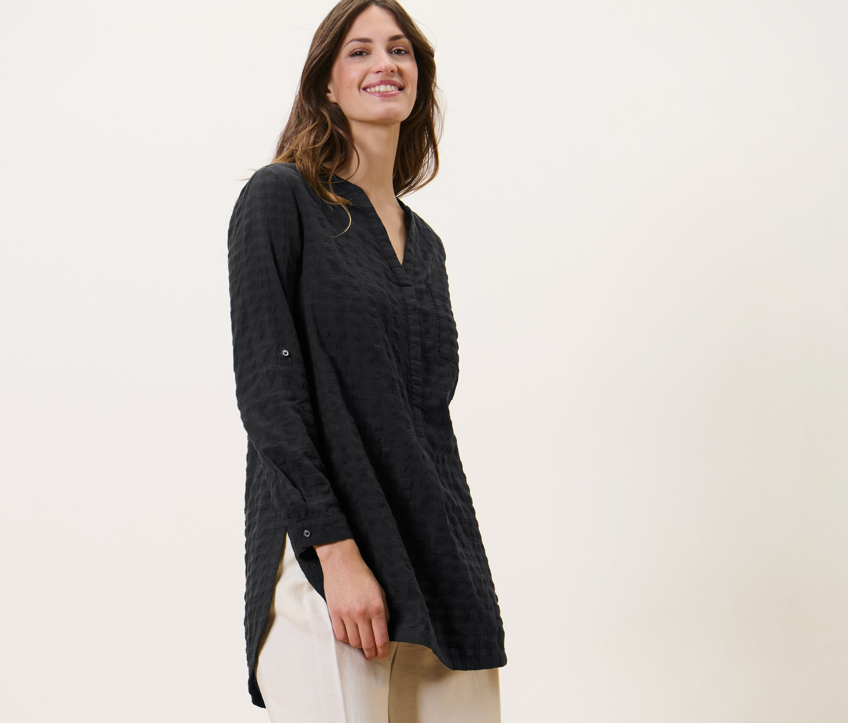 Kobieta ma na sobie długa tunika o strukturze tkaniny i jasne spodnie.