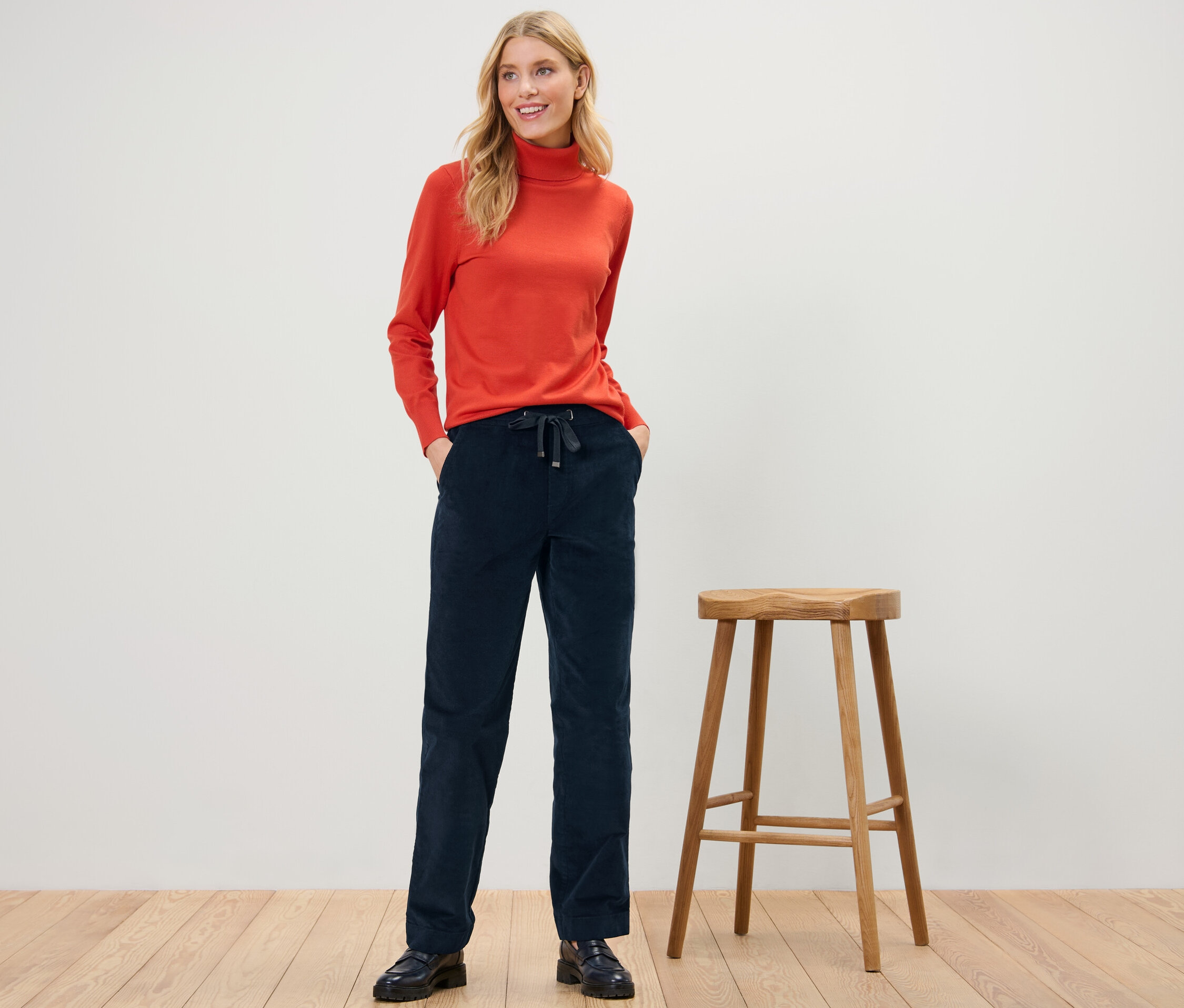 Kobieta pozuje w sztruksowych joggerach i pomarańczowym golfie.