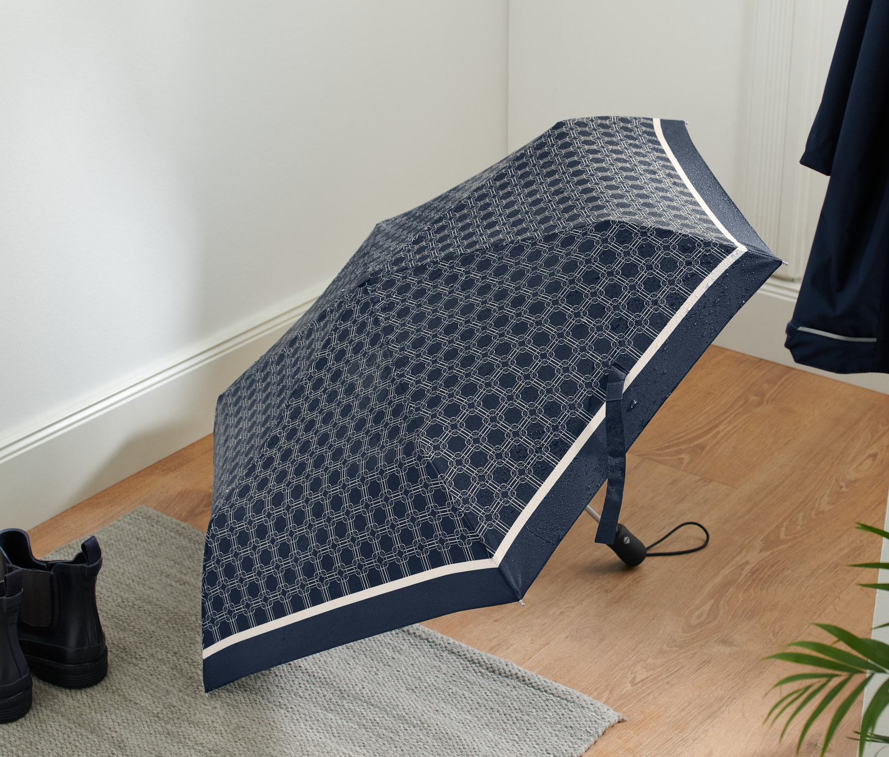 Otwarty kieszonkowy parasol automatyczny z geometrycznym wzorem leży na podłodze obok butów.