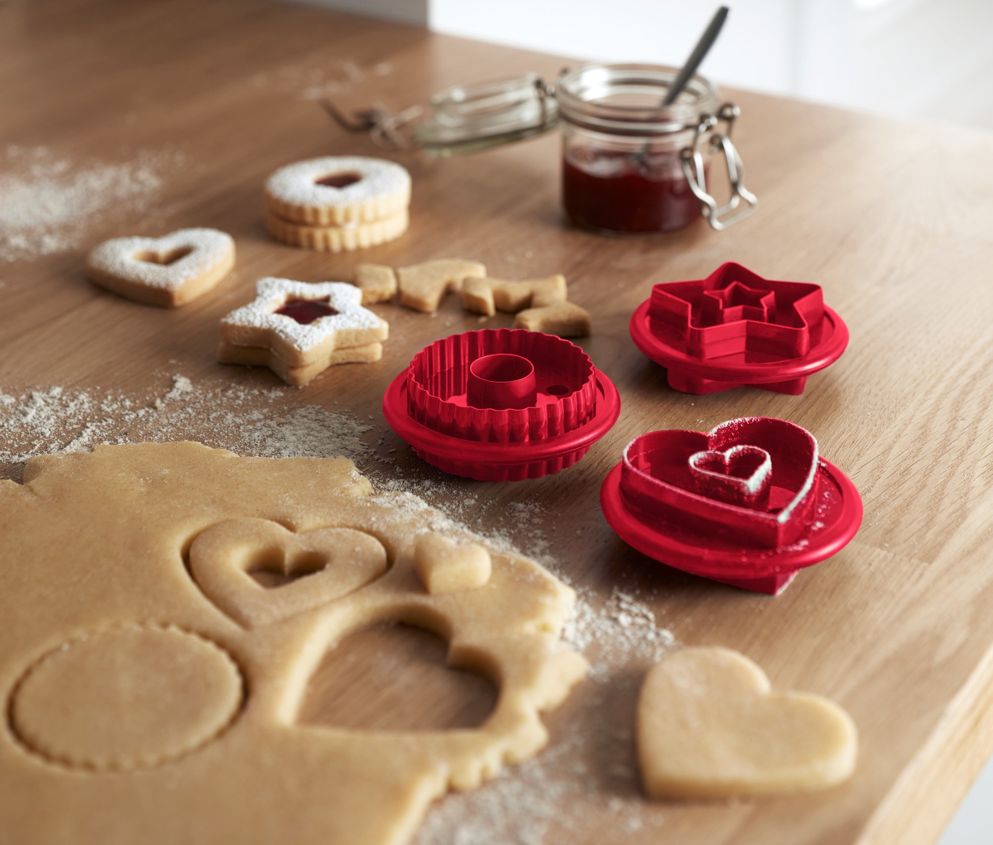 Na drewnianym stole leżą ciasteczka linzer i foremki do wycinania ciasteczek, 3 sztuki.