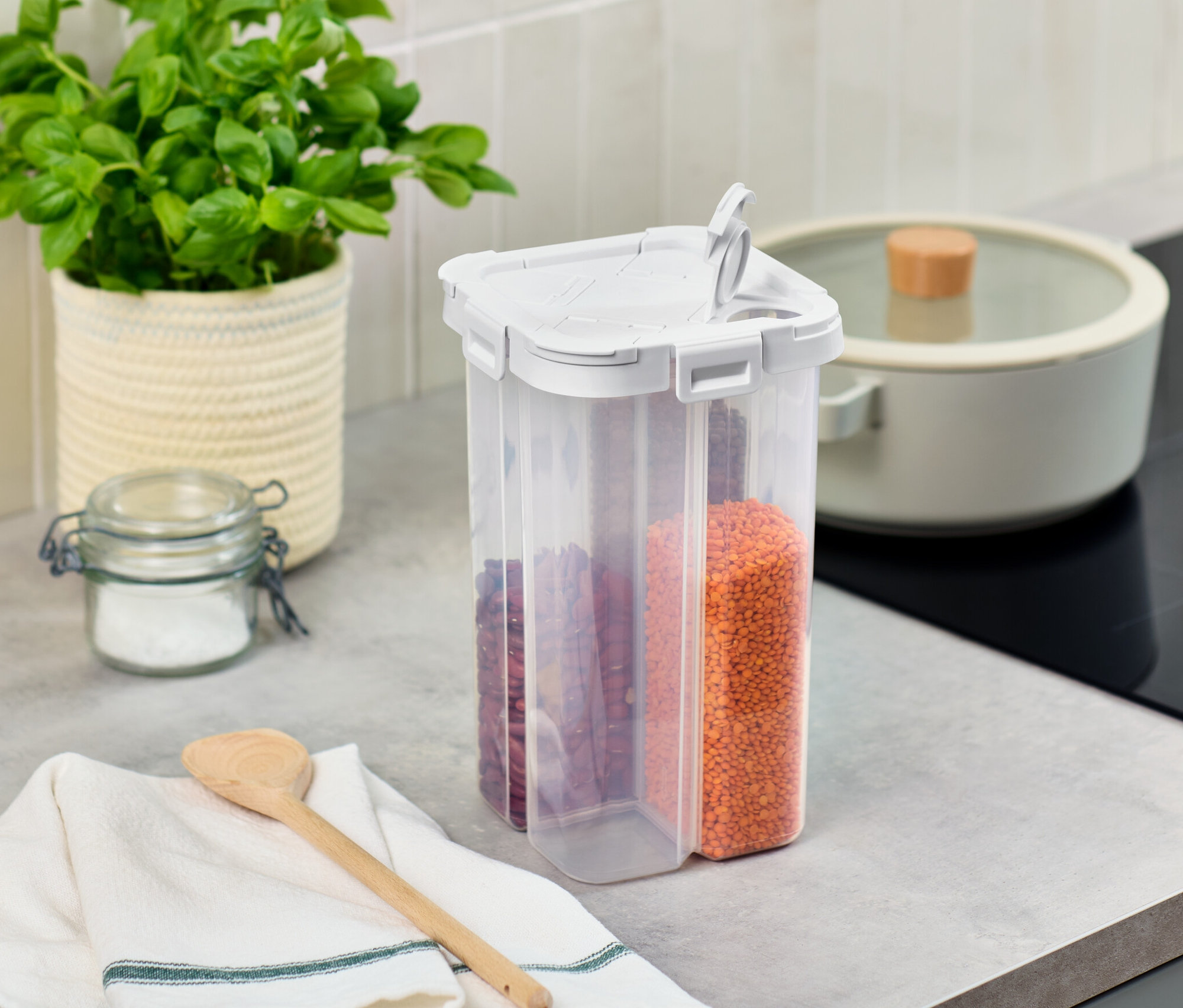 Na blacie kuchennym stoi pojemnik na żywność 4 w 1, doniczka z bazylią i szklany słoik.