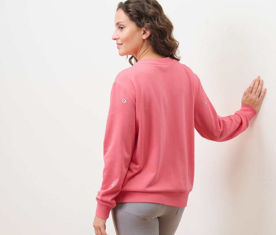 Kobieta ma na sobie haftowaną bluzę i szare spodnie.