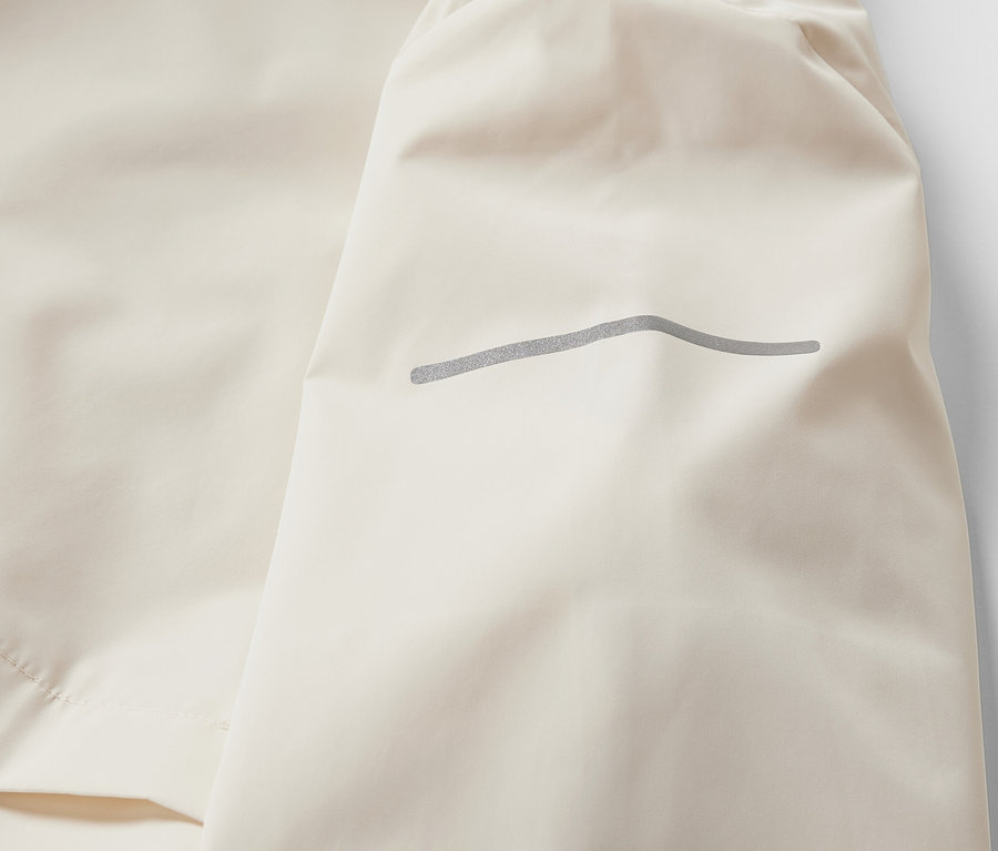 Zbliżenie kremowej, wiatroszczelnej kurtki do biegania.