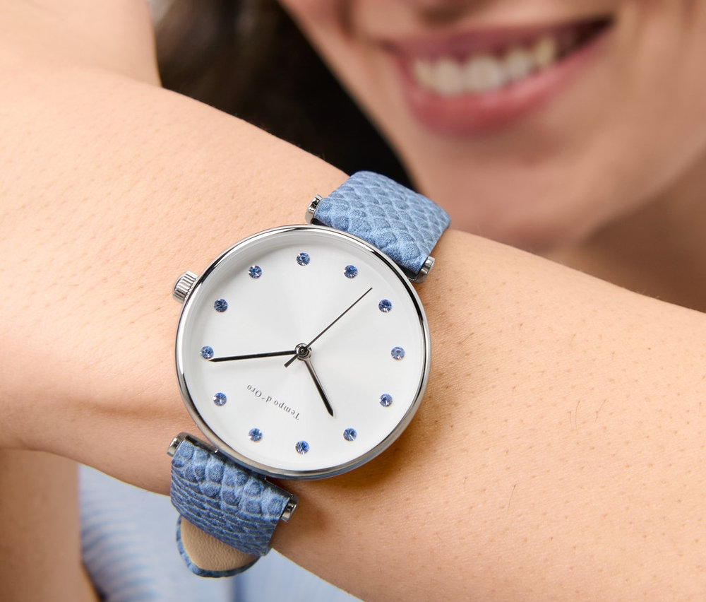 Uśmiechnięta kobieta nosi na nadgarstku zegarek na rękę ze skórzanym paskiem i kryształkami.