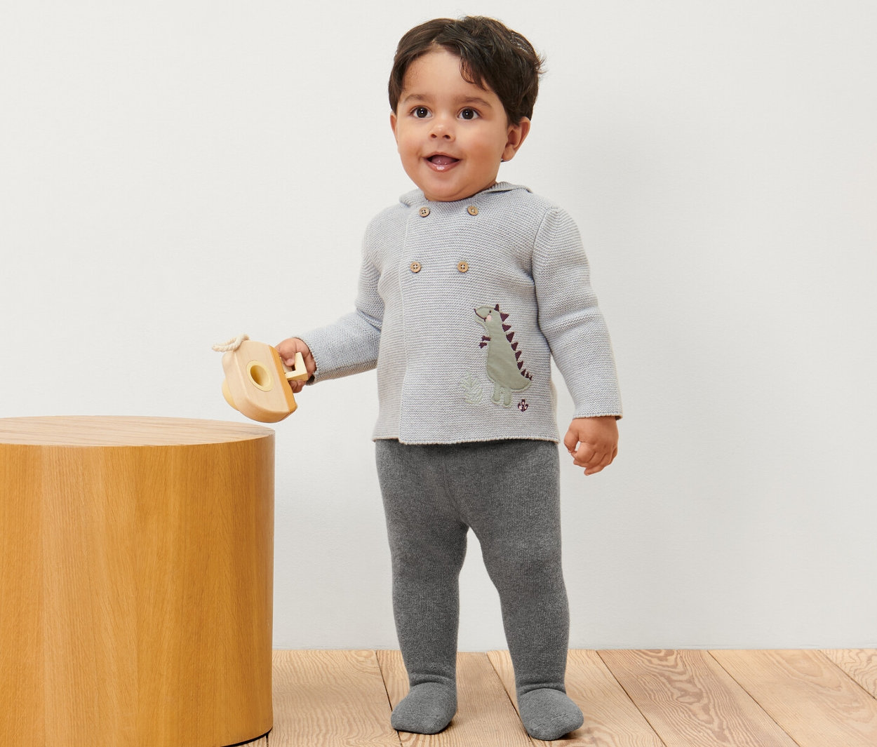 Chłopiec stoi i trzyma drewnianą zabawkę, ubrany w Dziecięce rajstopy termoaktywne, 2 pary, melanż.