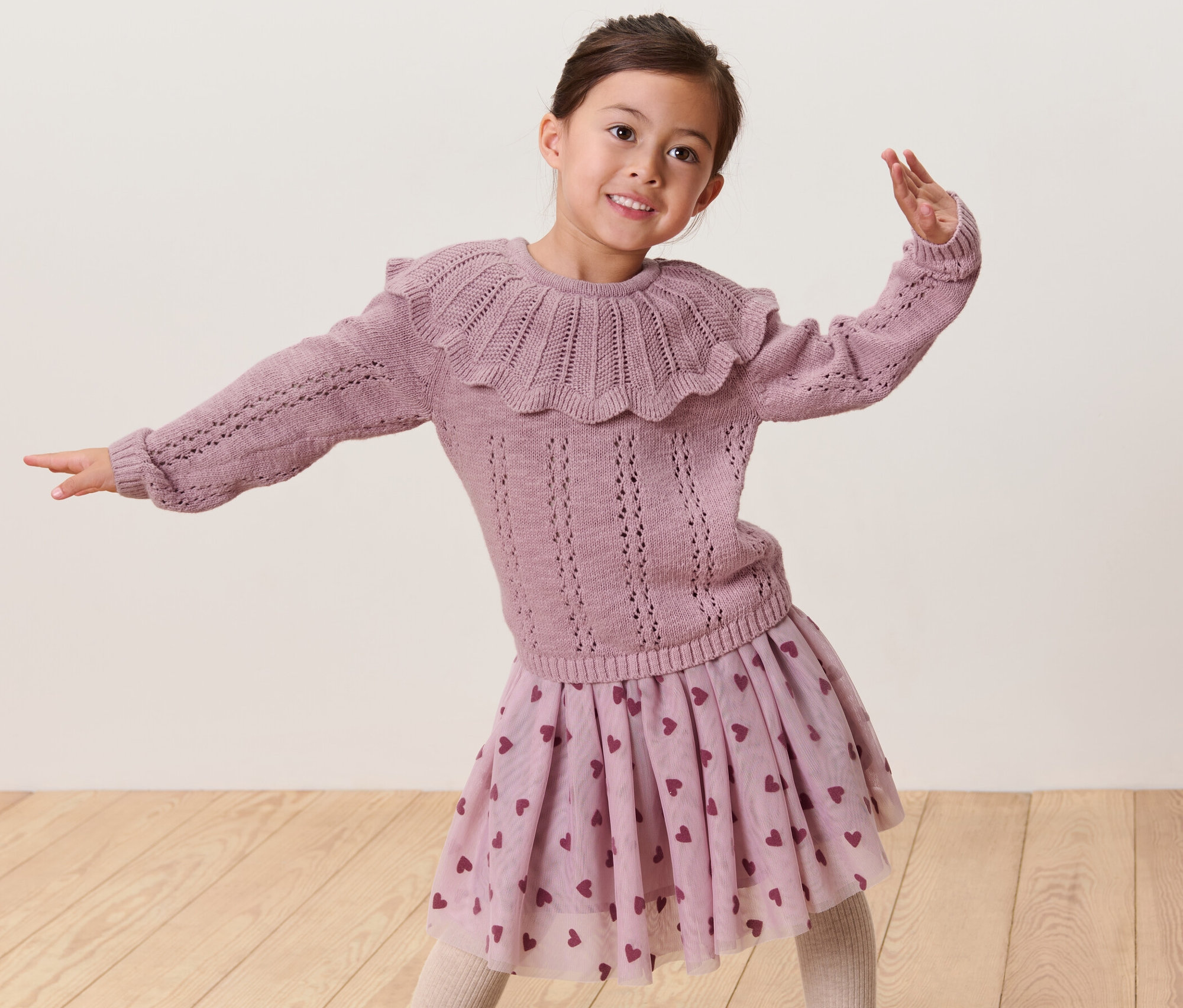 Uśmiechnięta dziewczyna pozuje w swetrze z kołnierzem i spódnicy w serduszka.