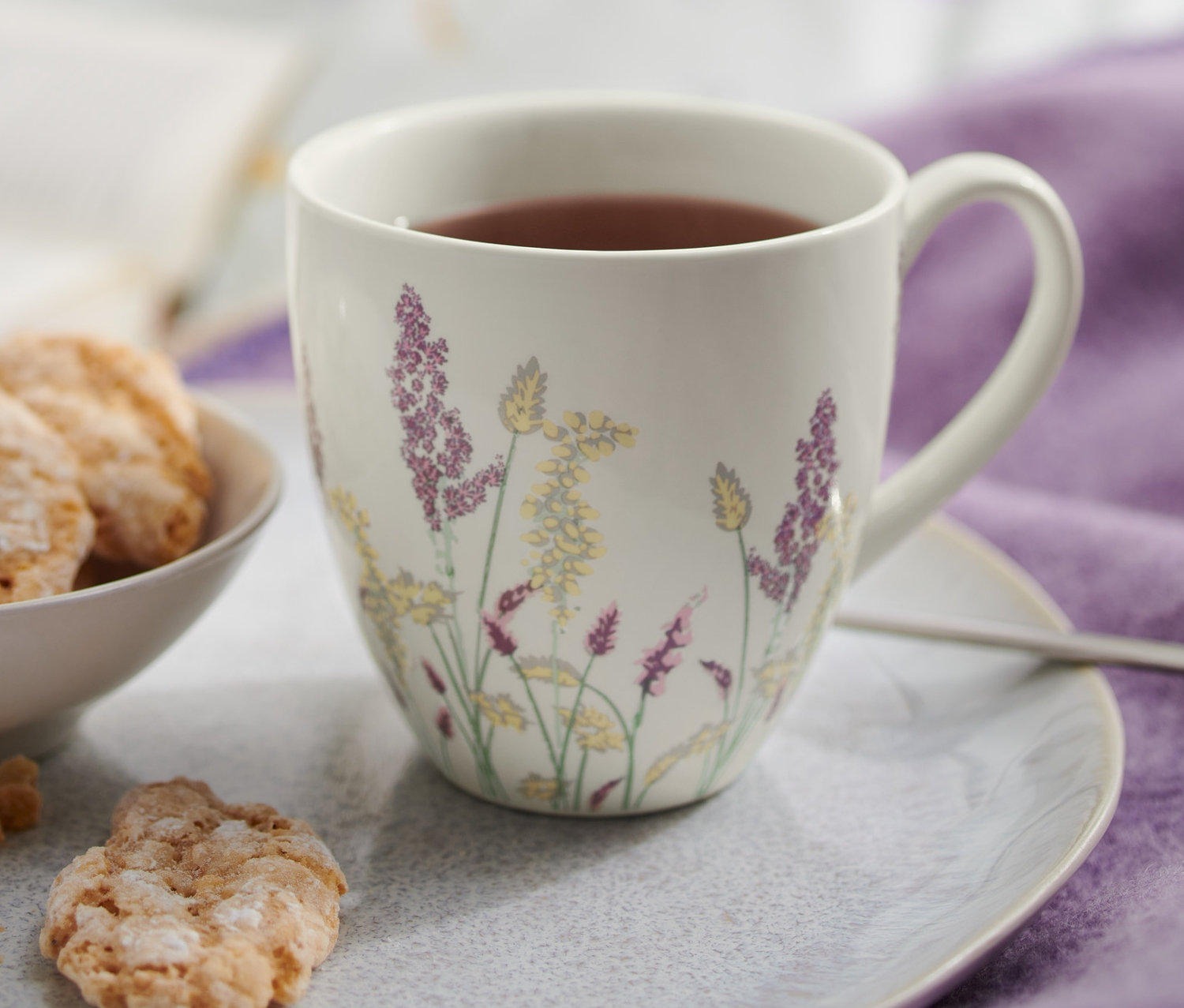 Pomarańczowe ciastka w misce i kubek z kwiatowym wzorem na talerzu.