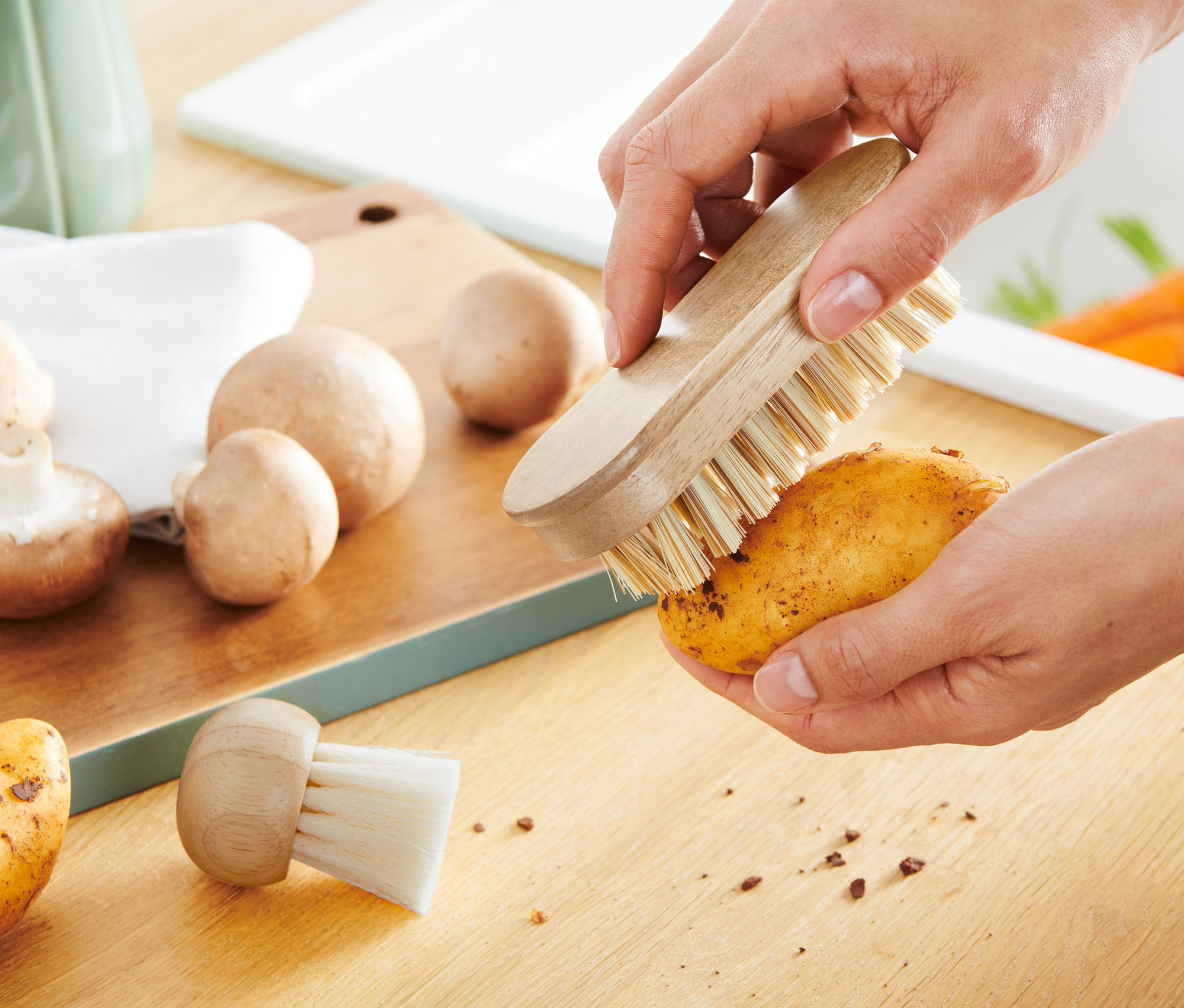 Osoba czyści ziemniaka za pomocą 2 szczoteczek do czyszczenia warzyw.