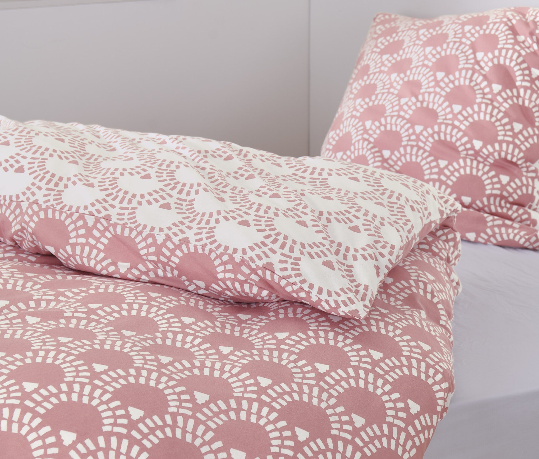 Zbliżenie na różową pościel z dżerseju we wzory. W tle widoczne są dwa wiklinowe kosze i książki.