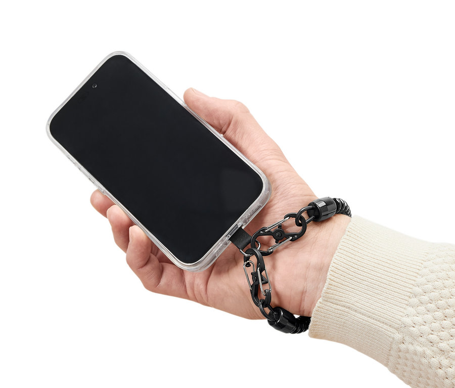 Ręka trzyma telefon w przezroczystym etui z czarnym łańcuszkiem zabezpieczającym do smartfona.