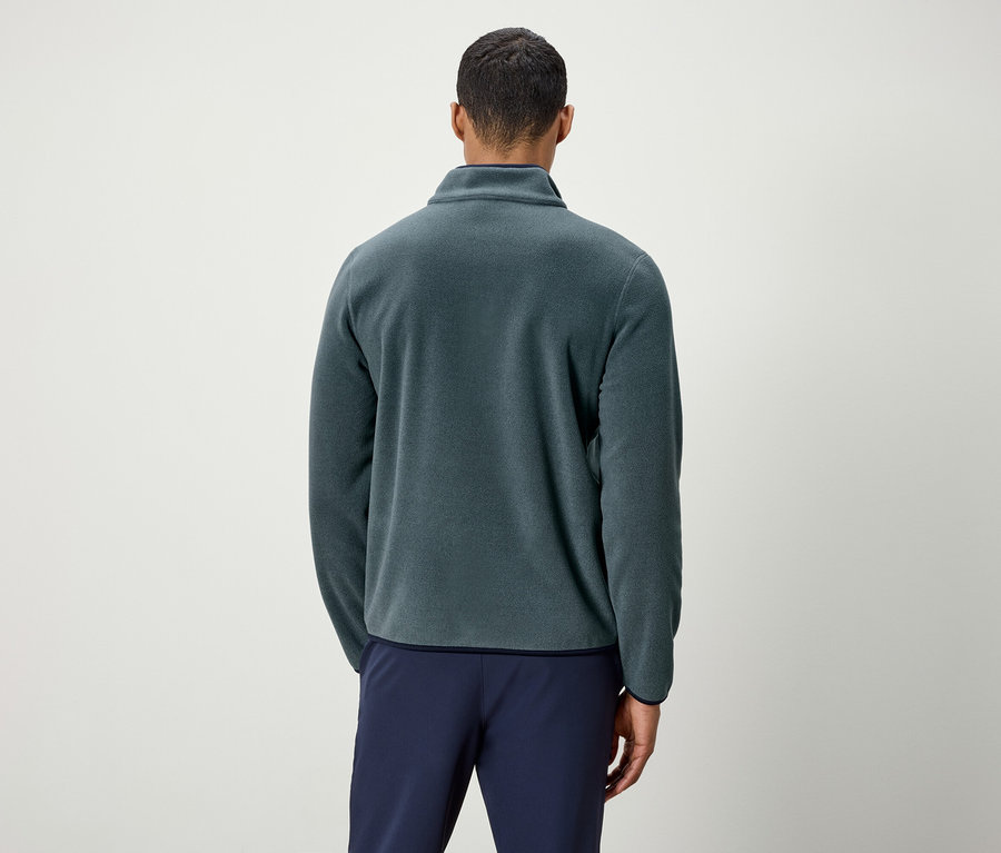 Mężczyzna tyłem do kamery w zielonej bluzie polarowej i niebieskich spodniach.