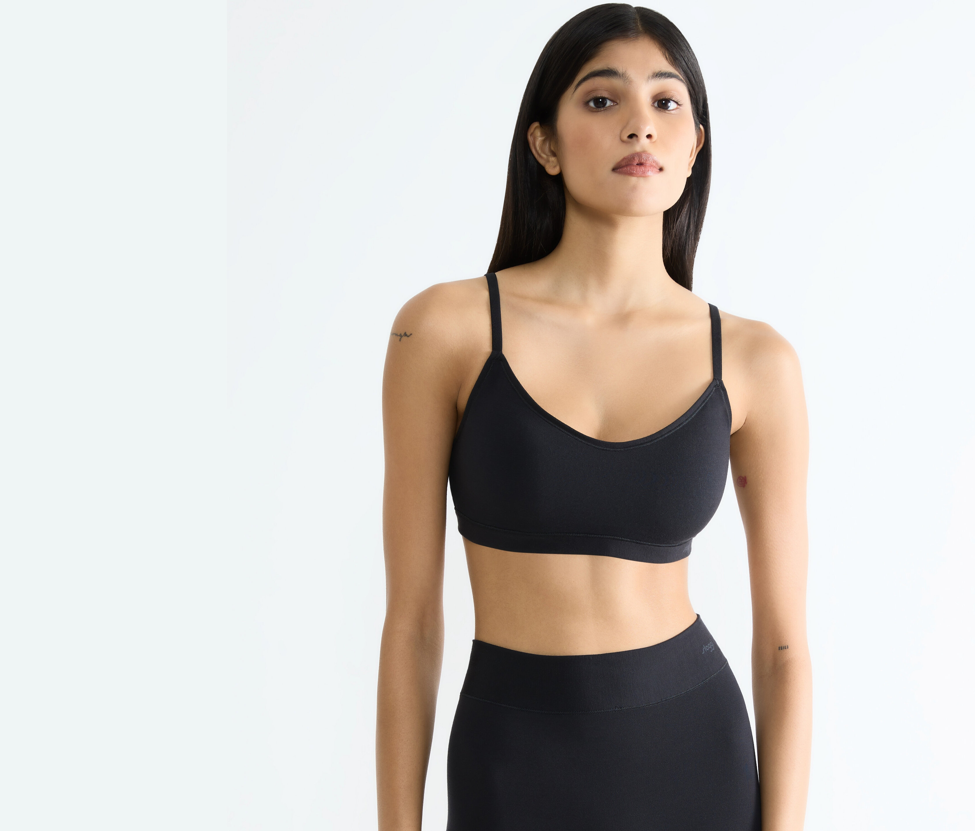 Kobieta w czarnym sportowym topie i legginsach pozuje na białym tle.