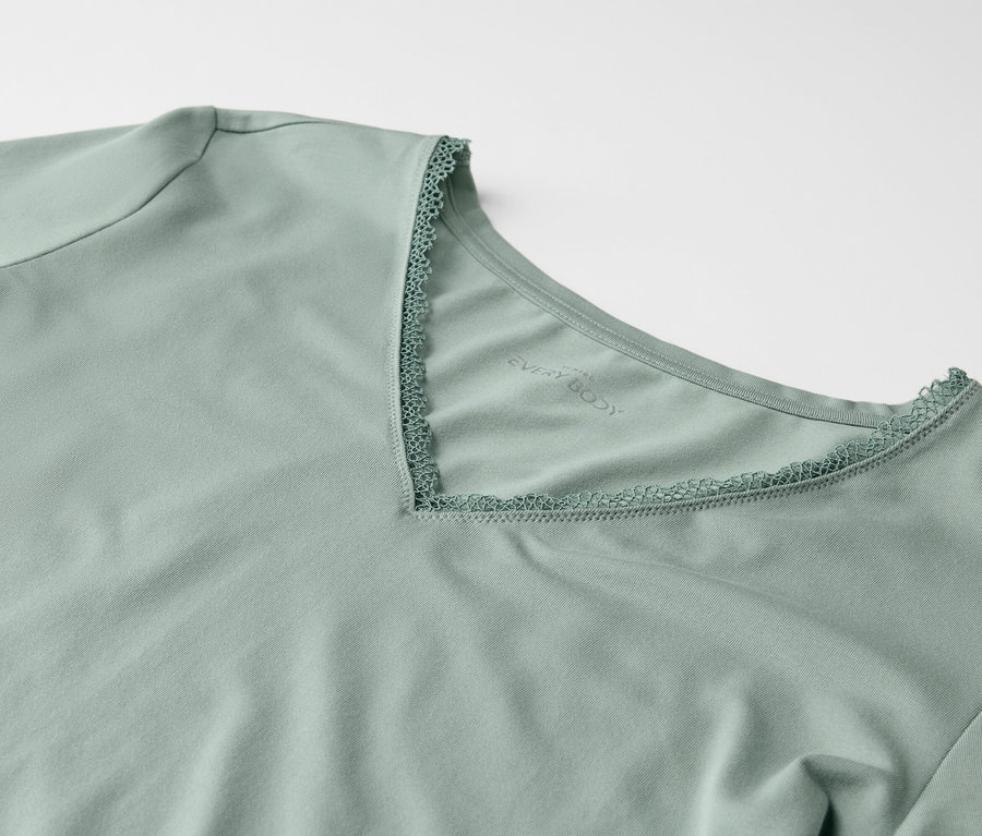 Zbliżenie jasnozielonej koszulki z krótkim rękawem i dekoltem w kształcie litery V obszytym koronką.