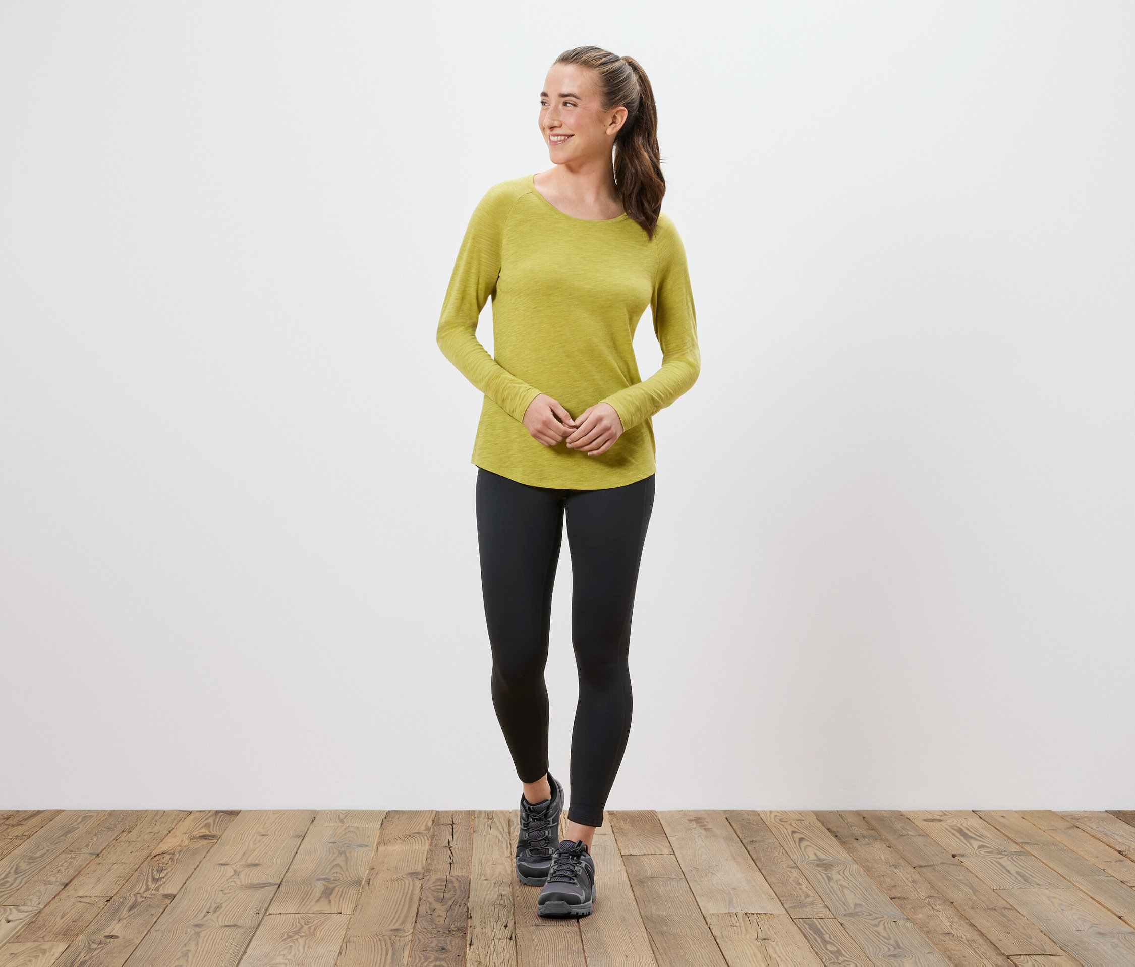 Kobieta w żółto-zielonej bluzce z długim rękawem, czarnych legginsach i szarych butach.