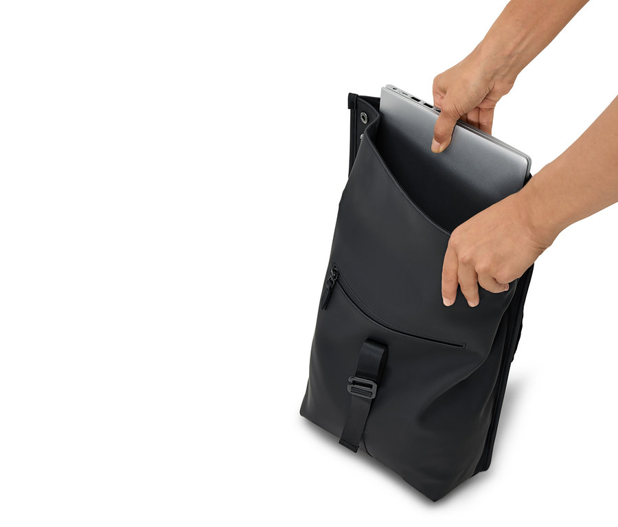 Ręce wkładają srebrny laptop do otwartego czarnego plecaka.