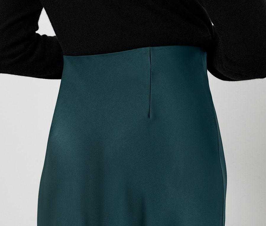 Widok z tyłu kobiety w czarnej bluzce i zielonej spódnicy.