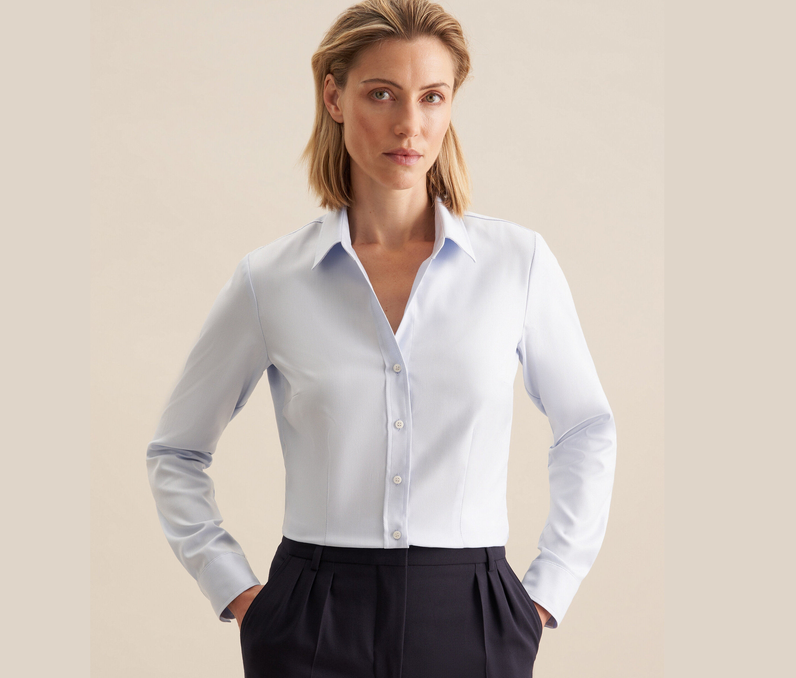 Kobieta ma na sobie jasnoniebieską koszulę z twillu Seidensticker i granatowe spodnie.