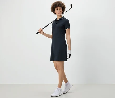 Kobieta trzyma kij golfowy na ramieniu i ma na sobie sukienkę sportową.
