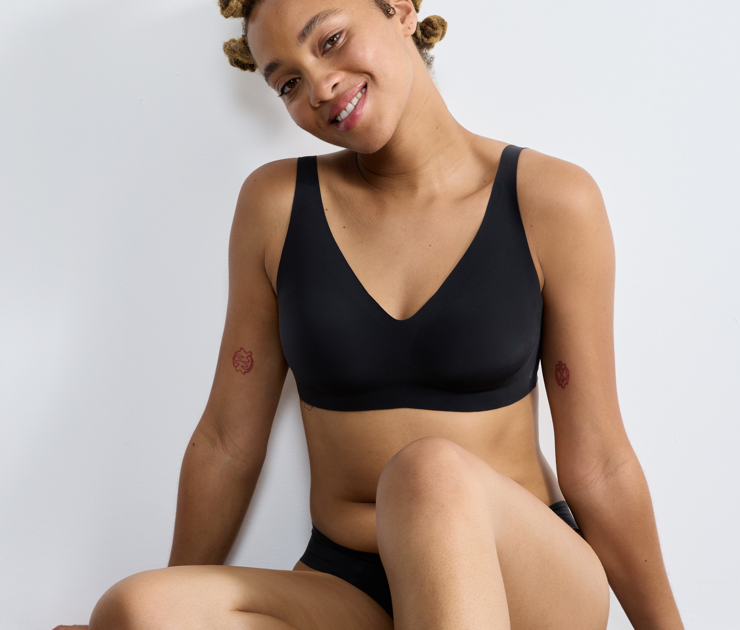 Kobieta siedzi i ma na sobie czarny miękki biustonosz sloggi ZERO Feel 2.0.