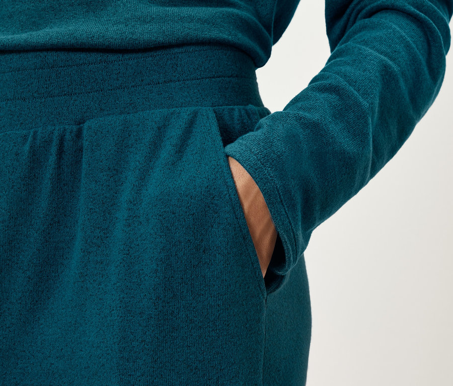 Zbliżenie na kobietę w granatowych spodniach dresowych z ręką w kieszeni.