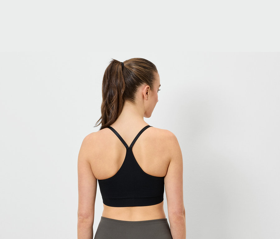 Widok z tyłu kobiety w kucyku, ubranej w czarny biustonosz sportowy i szare legginsy.