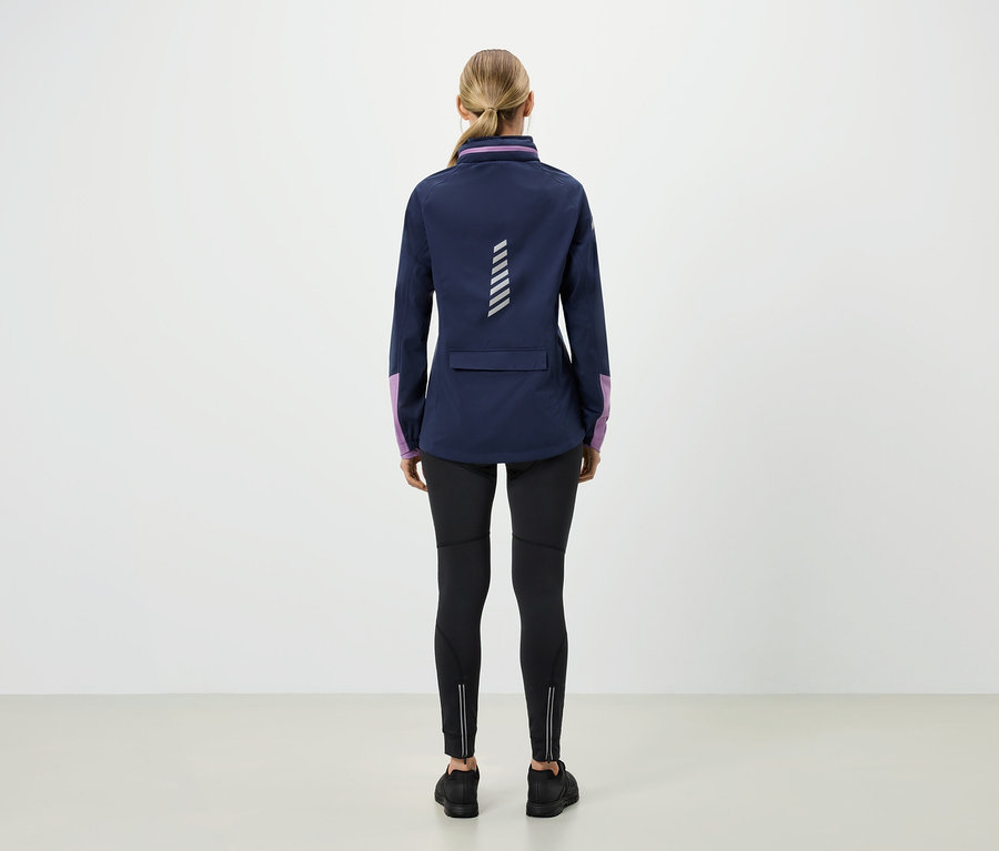 Widok z tyłu blondynki w niebieskiej kurtce z fioletowymi rękawami, czarnych legginsach i czarnych butach.