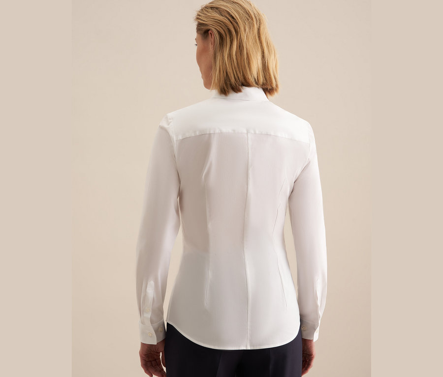 Widok z tyłu na kobietę z krótkimi blond włosami w białej koszuli slim fit Seidensticker i granatowych spodniach.