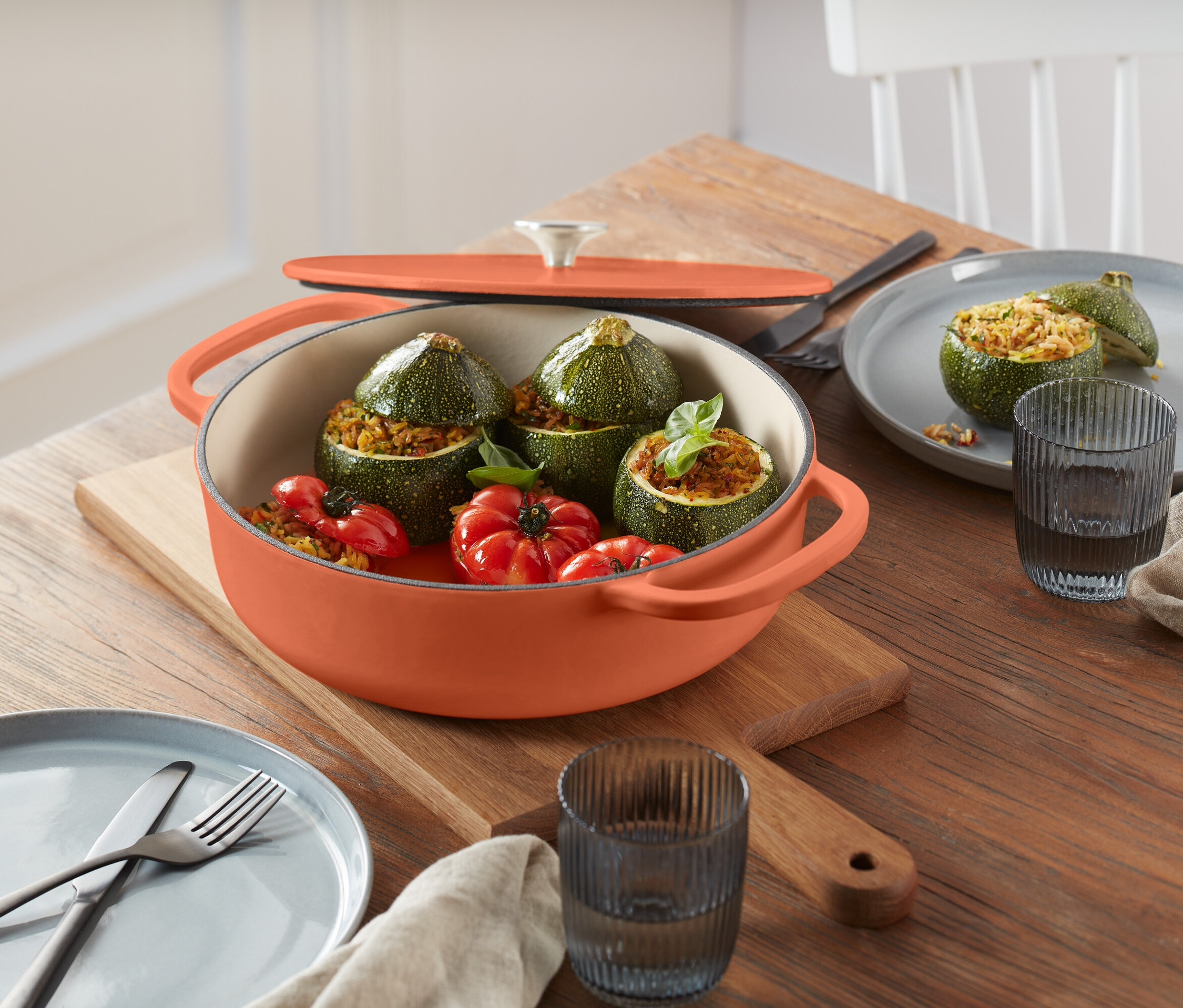 Faszerowane cukinie i pomidory w pomarańczowym garnku na drewnianej desce do krojenia.