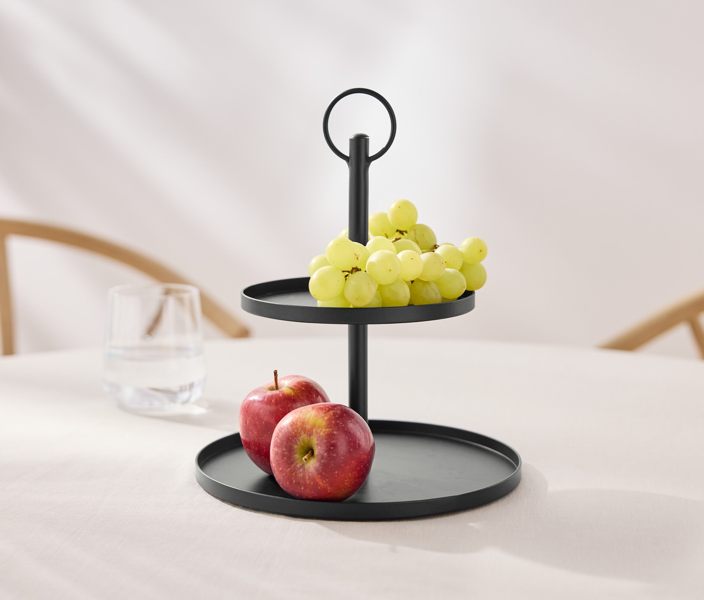 Dwupoziomowa czarna etażerka z winogronami i jabłkami na stole.