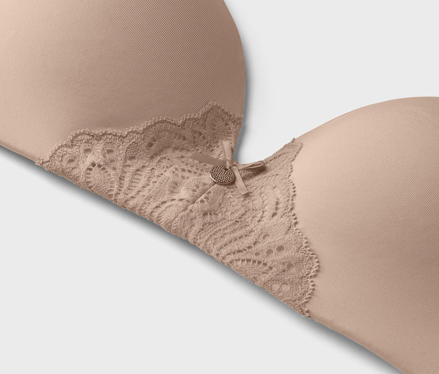 Zbliżenie beżowego biustonosza z koronkowym wykończeniem i małym ozdobnym guzikiem.