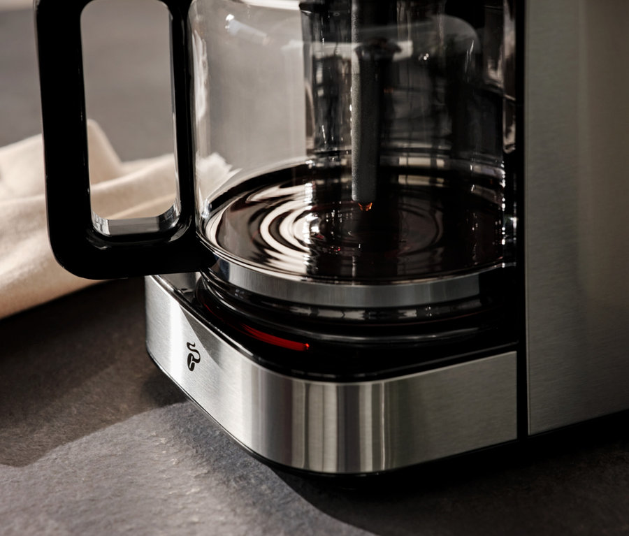 Szczegółowy widok ekspresu do kawy z dzbankiem i beżową ściereczką w tle.