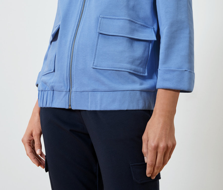 Kobieta nosi jasnoniebieską kurtkę i ciemnoniebieskie spodnie.