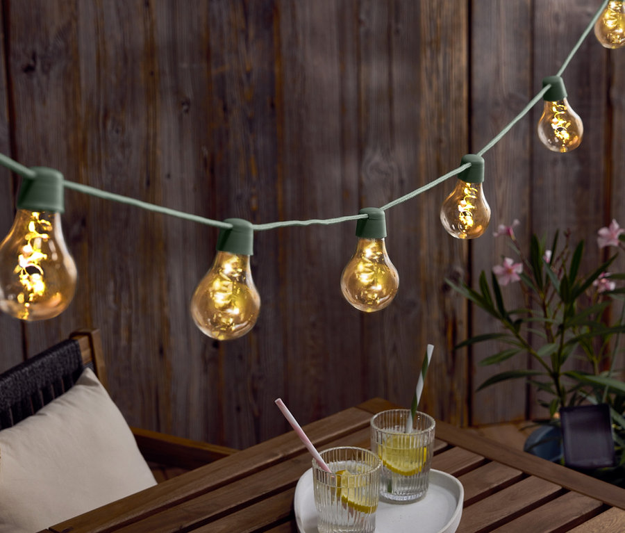Girlanda świetlna z żarówkami zwisa nad drewnianym stołem z napojami i kapeluszem.