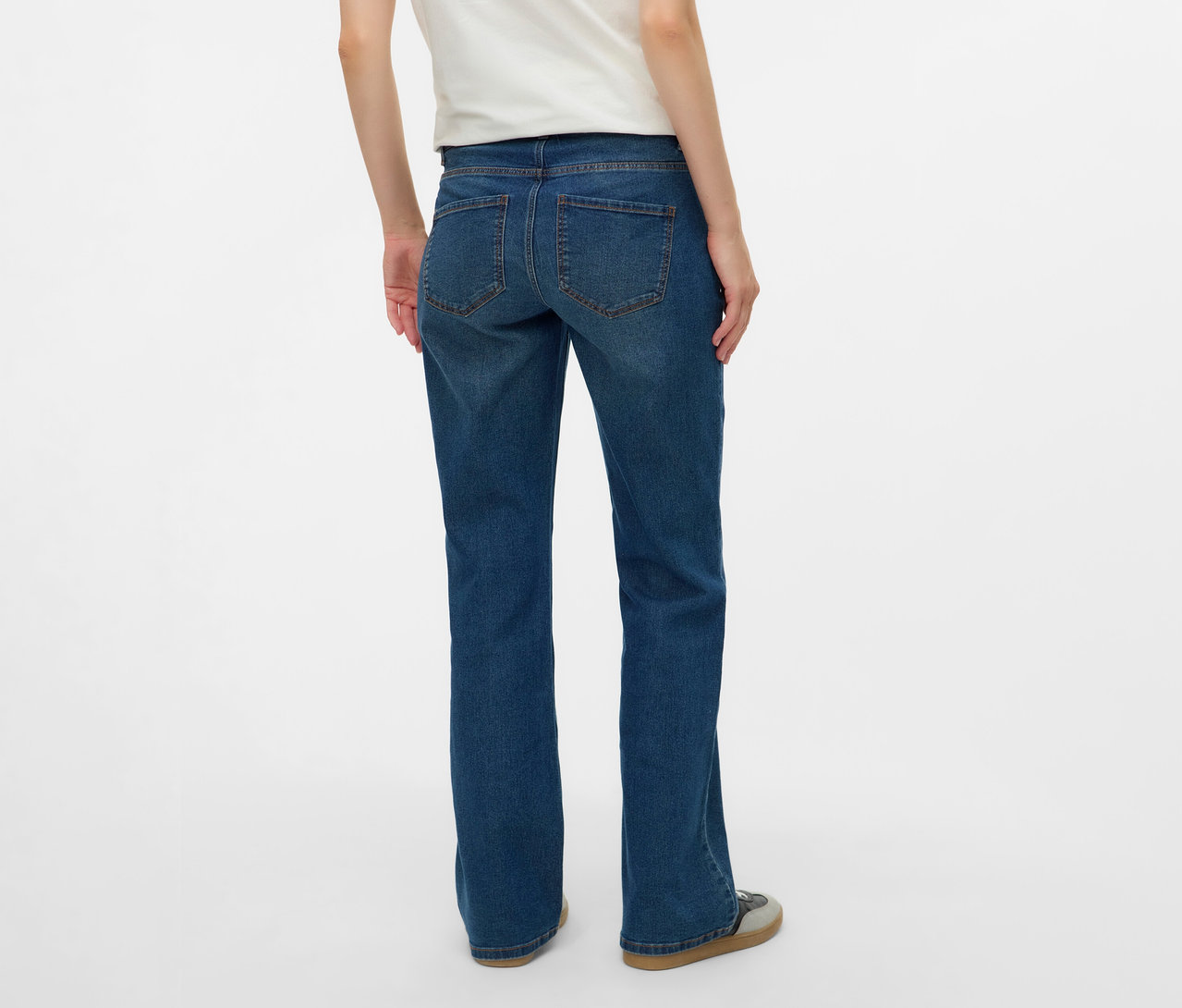 Widok z tyłu kobiety w białej koszulce i rozszerzanych jeansach MAMALICIOUS „MLEDINA” na białym tle.