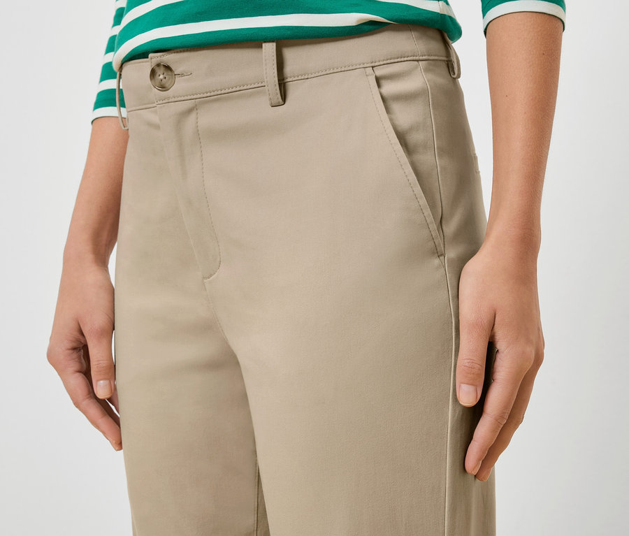 Zbliżenie kobiety w beżowych spodniach i bluzce w zielono-białe paski.