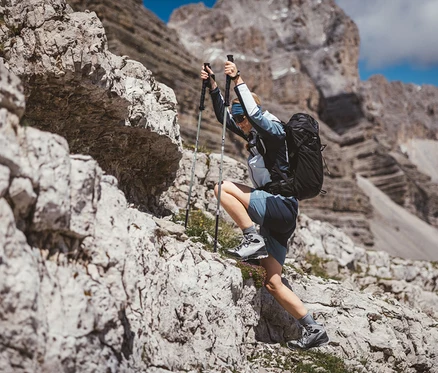 Kobieta wspina się po skałach z kijkami trekkingowymi CMP i plecakiem trekkingowym CMP HAVRE, 40 litrów.