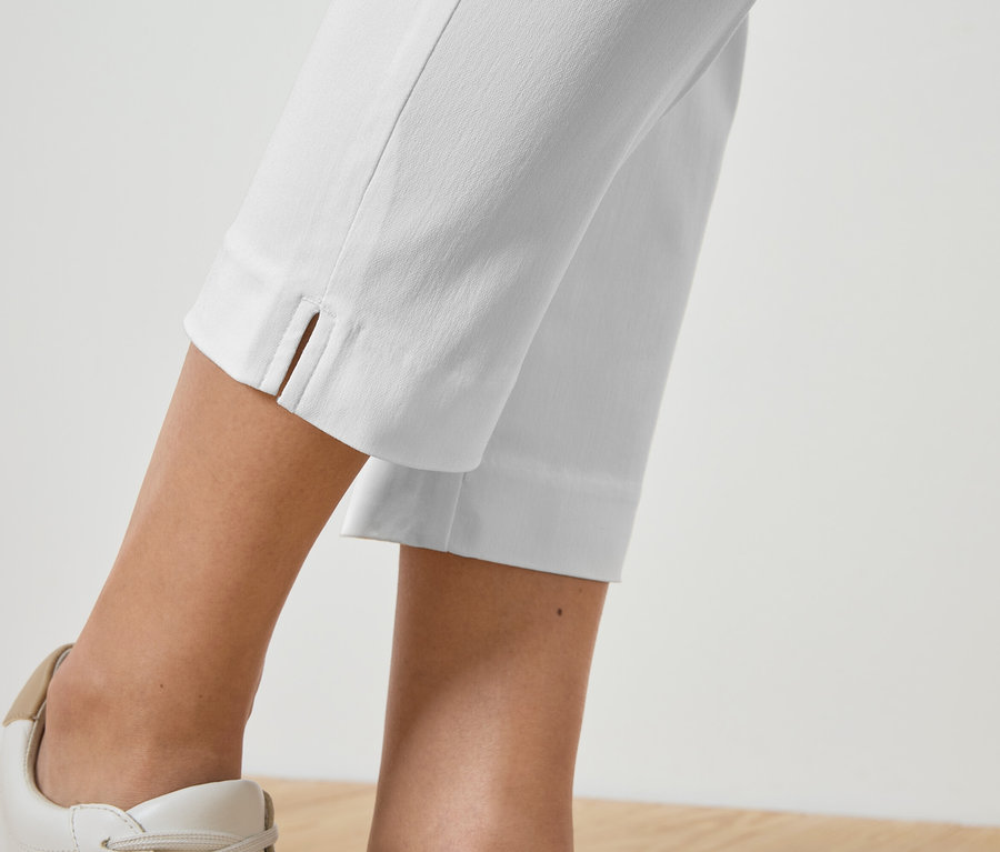 Zbliżenie na nogi osoby ubranej w białe spodnie i pasujące do nich tenisówki.