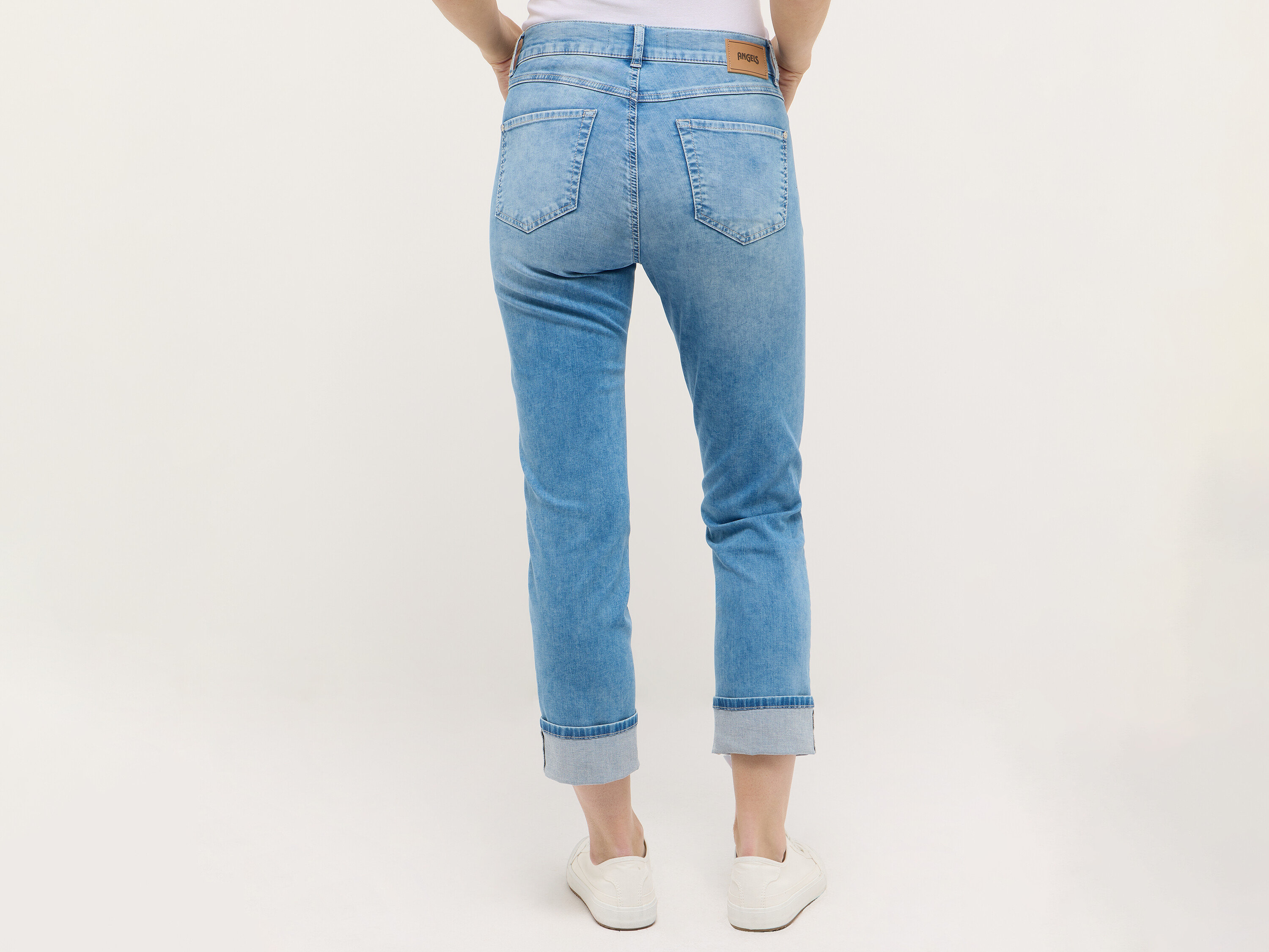 Biodra i nogi kobiety w jasno niebieskich jeansach i białych trampkach, widok z tyłu.