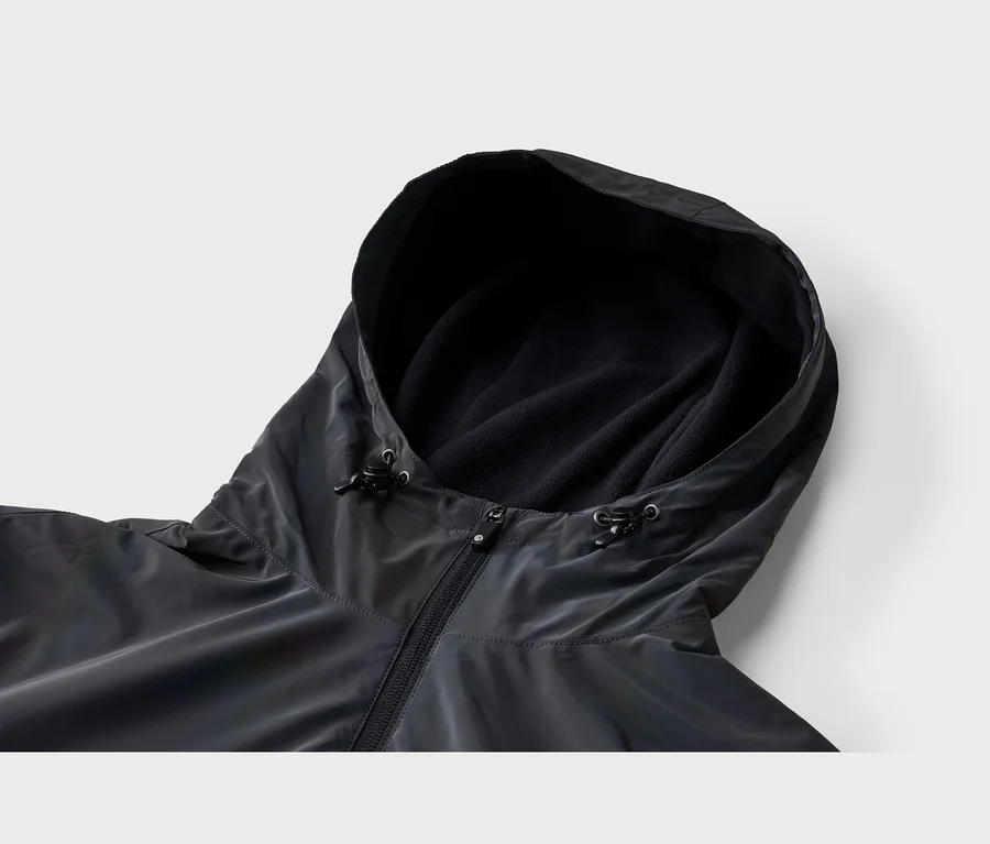 Zbliżenie ciemnej, prawdopodobnie opalizującej kurtki z kapturem. Kaptur jest wyściełany czarnym polarem i ma regulowane sznurki. Z przodu widoczny jest czarny zamek błyskawiczny.