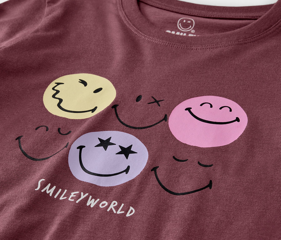 Zbliżenie na fioletową piżamę dziecięcą SMILEYWORLD® z nadrukiem twarzy.