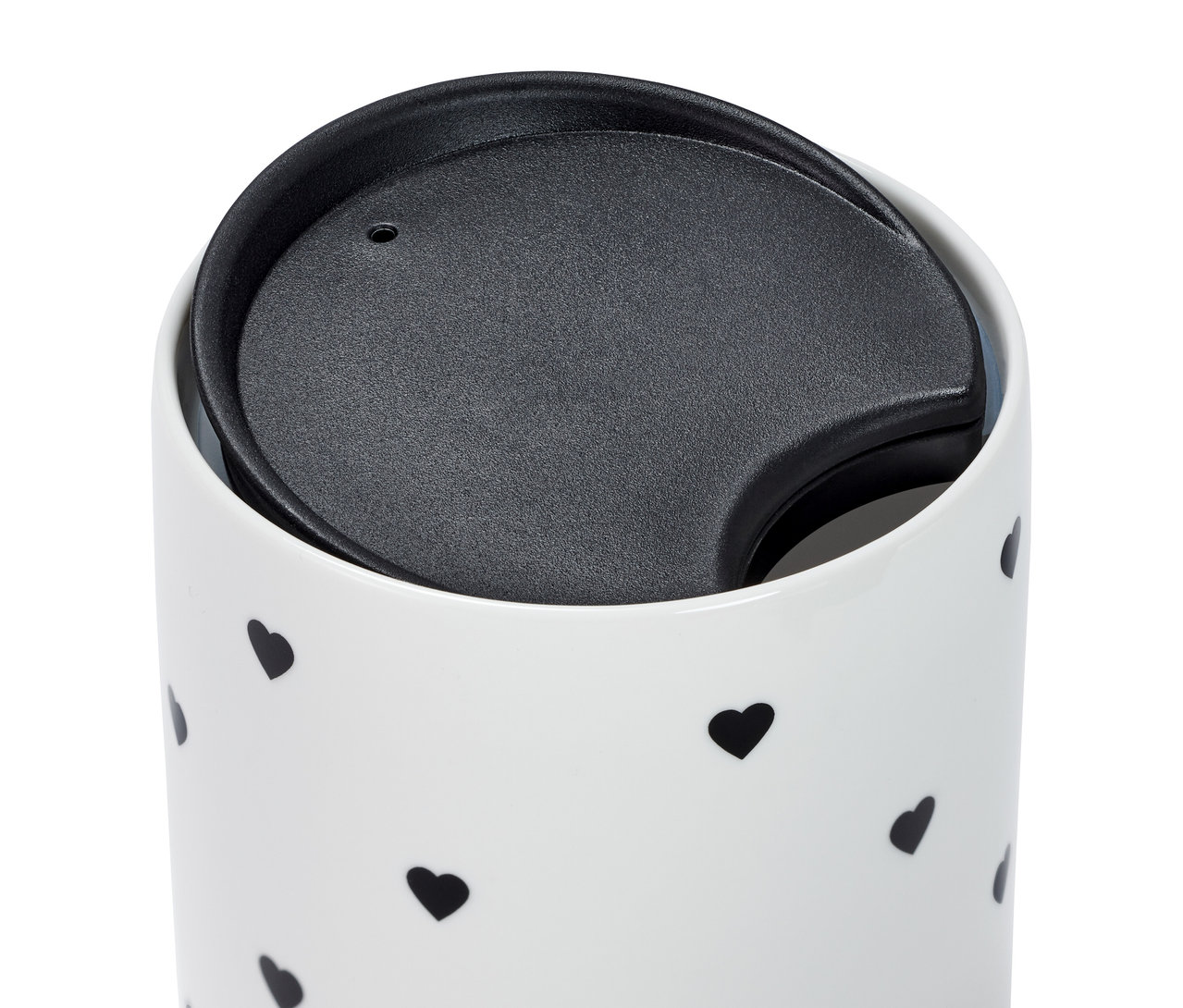 Zbliżenie na porcelanowy kubek z pokrywką i czarnymi serduszkami.