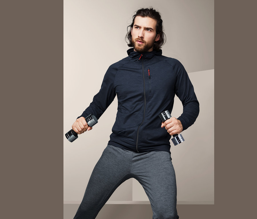 Mężczyzna ćwiczy z hantlami i ma na sobie bluzę funkcyjną.