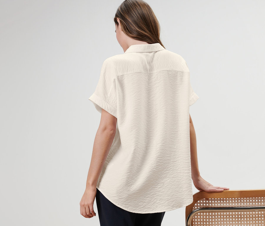 Kobieta stoi tyłem, ma na sobie bluzkę i opiera się o krzesło.