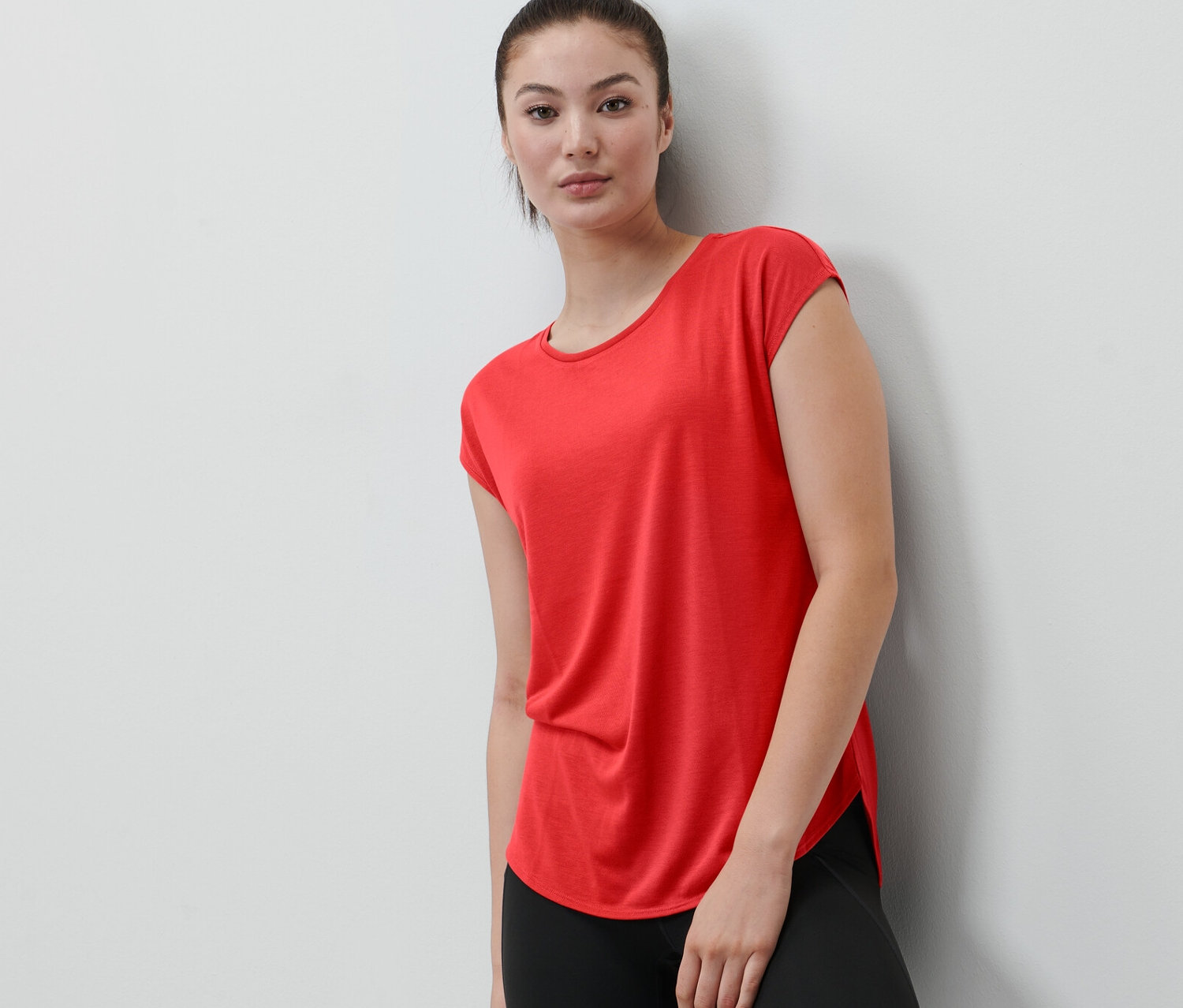 Kobieta oparta o ścianę ma na sobie czerwoną koszulkę sportową.