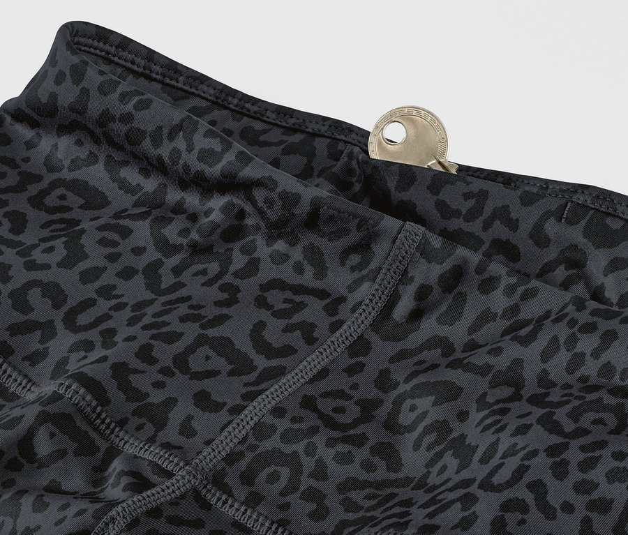 Szczegół szaro-czarnych legginsów sportowych we wzór w cętki z kluczem w kieszeni.