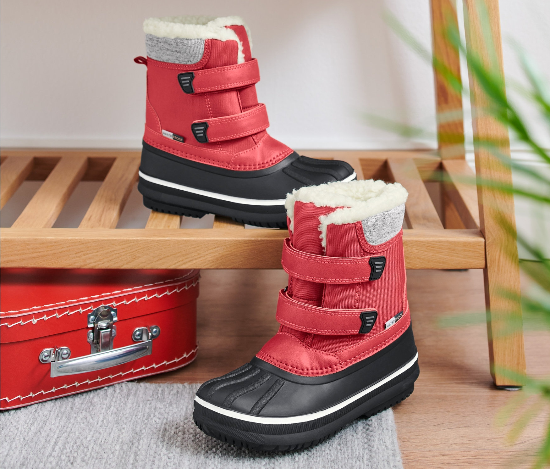 Dwa czerwone buty dziecięce na każdą pogodę stoją na drewnianej półce.